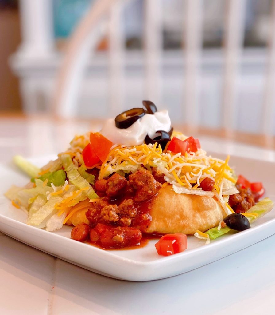 Navajo Taco on a white square plate loaded with all the toppings on a table.