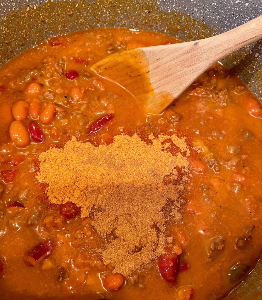 Ground beef browned with chili added, stirring in taco seasoning packets with wooden spoon.