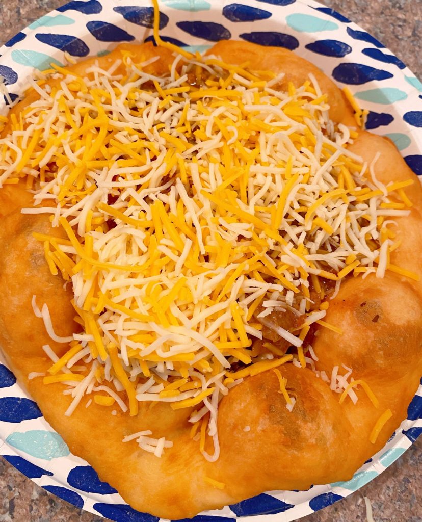 Adding cheese to meat filling on top of Navajo Tacos.