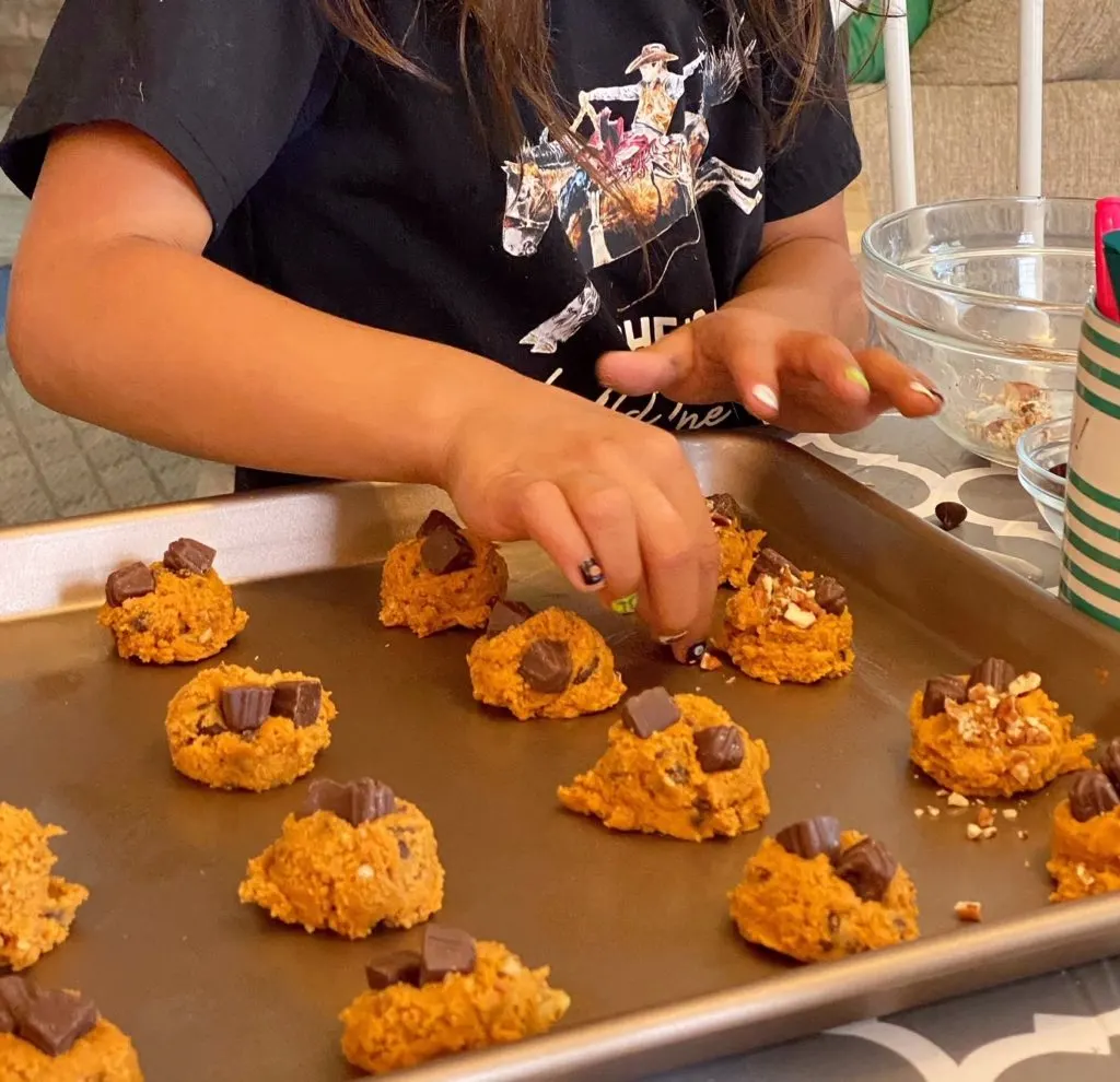 Topping each cookie dough ball with chocolate chips and nuts before baking.