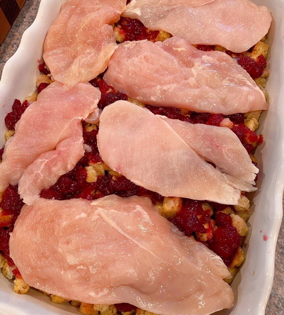 Chicken cutlets over stuffing and cranberries sauce in casserole dish.