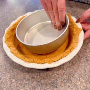 Pressing graham cracker crumbs inside the pie plate.
