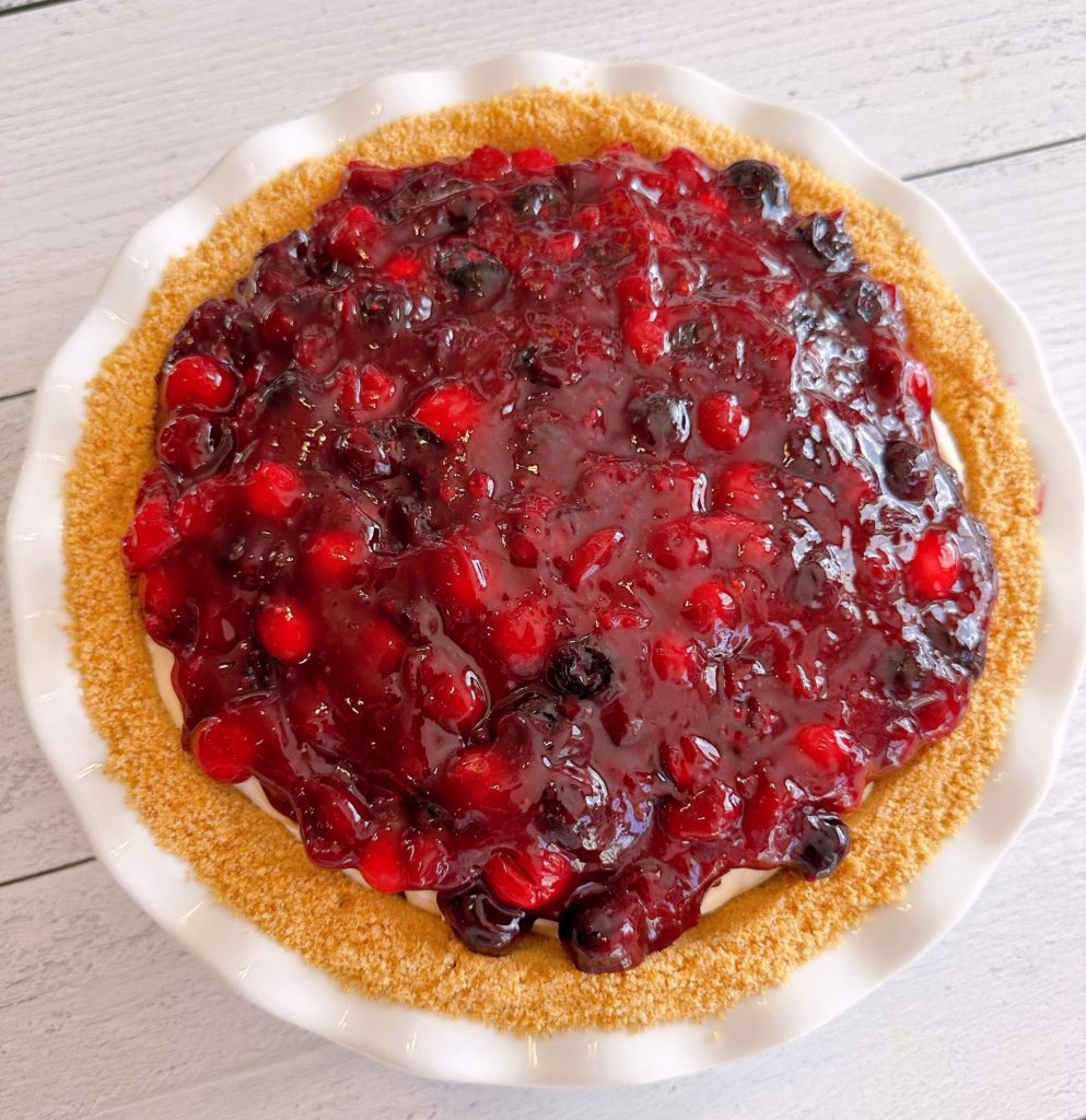 Cranberry Blueberry Pie with topping spread evenly over the cream cheese filling waiting for whipped cream to be piped around edges.