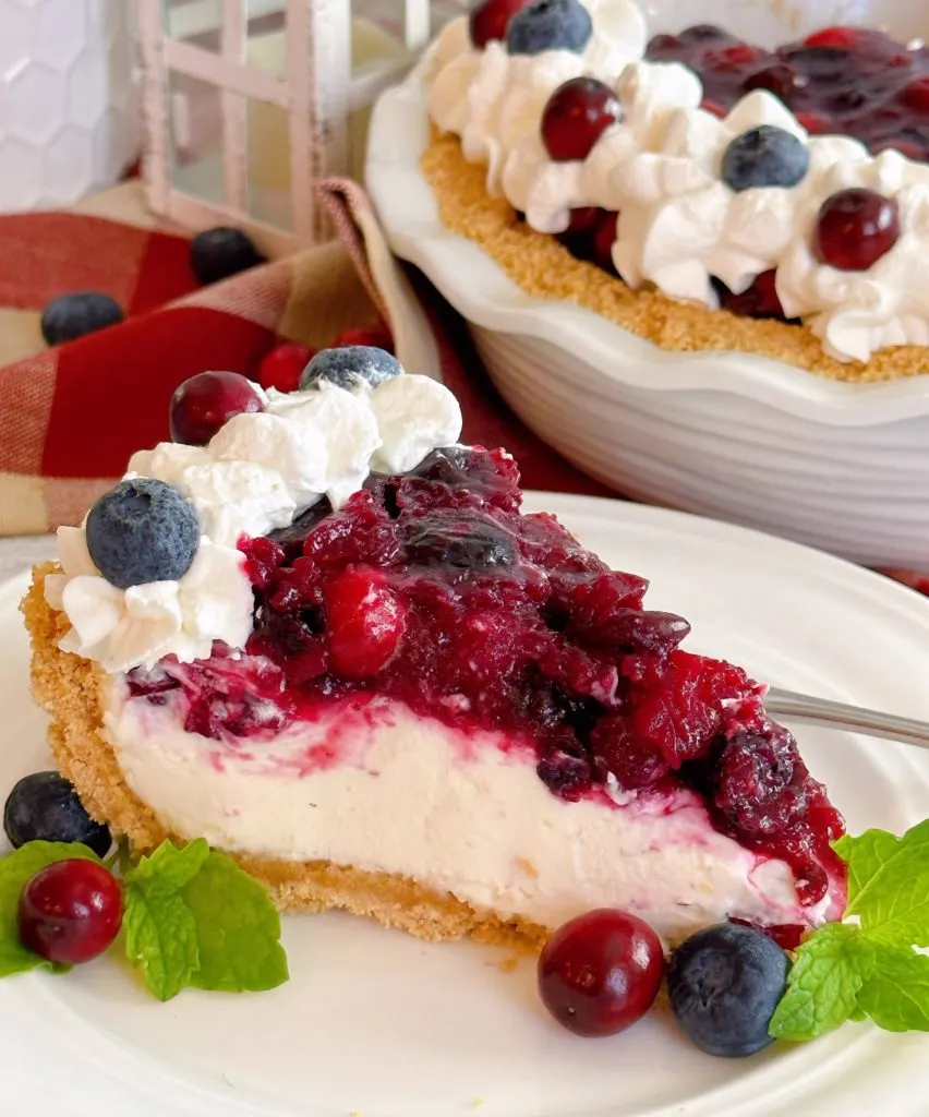 Cranberry Blueberry Cream Cheese Pie cut into a slice on a dessert plate and garnished with fresh berries and mint.
