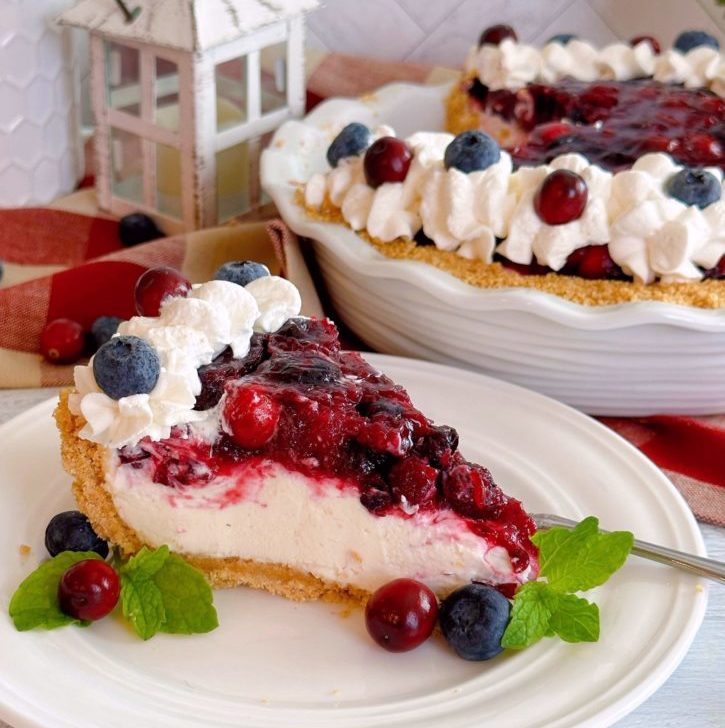 Slice of Cranberry Blueberry Cream Cheese Pie on a plate with the entire pie in the background.