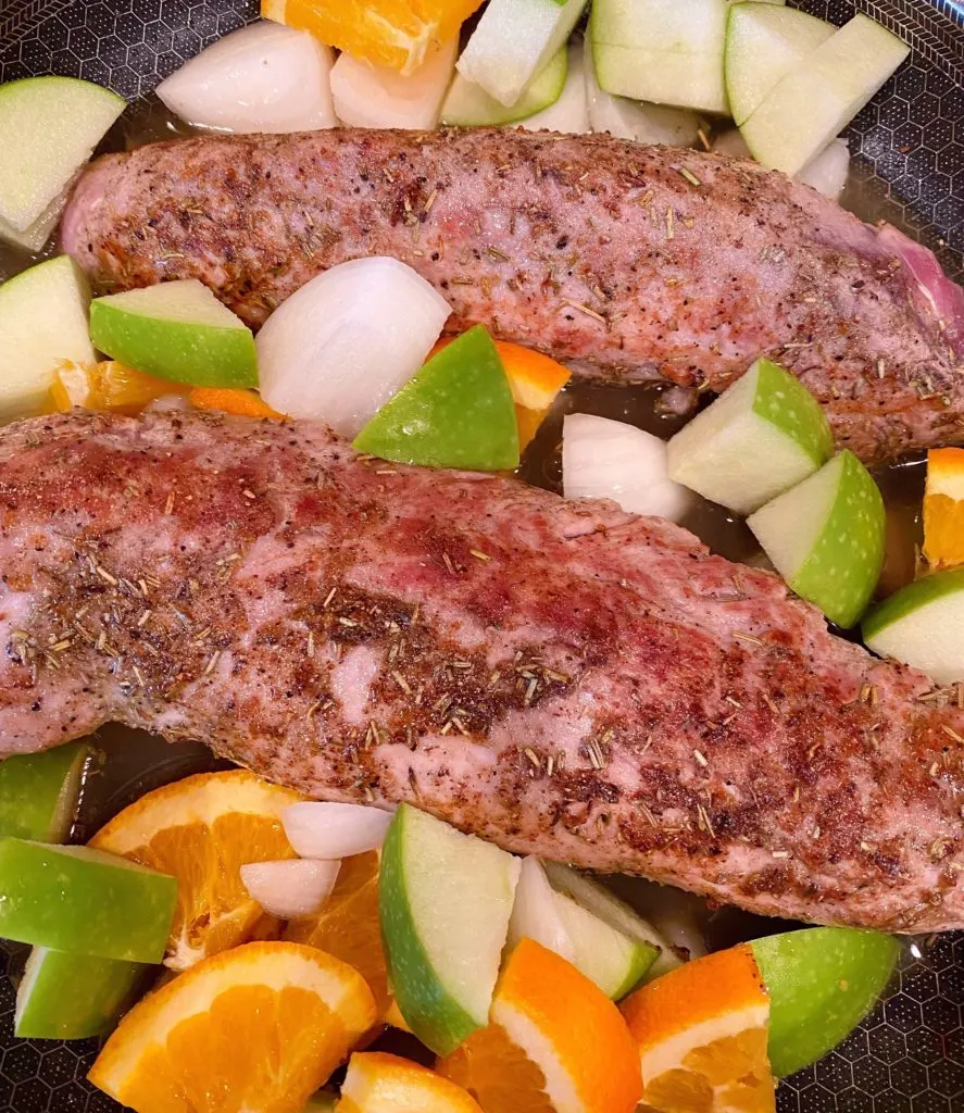 Adding apples, oranges and onions to pork tenderloin in skillet.