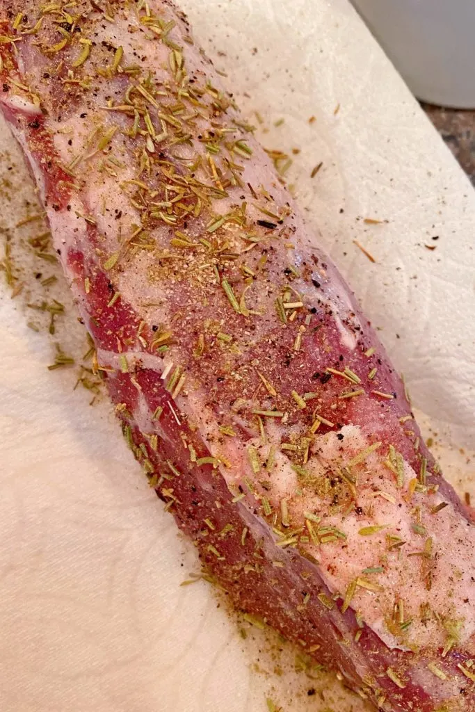 Pork Tenderloin seasoned with herbs on a paper towel.