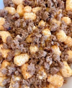 Topping frozen tater tots with browned sausage in baking dish.