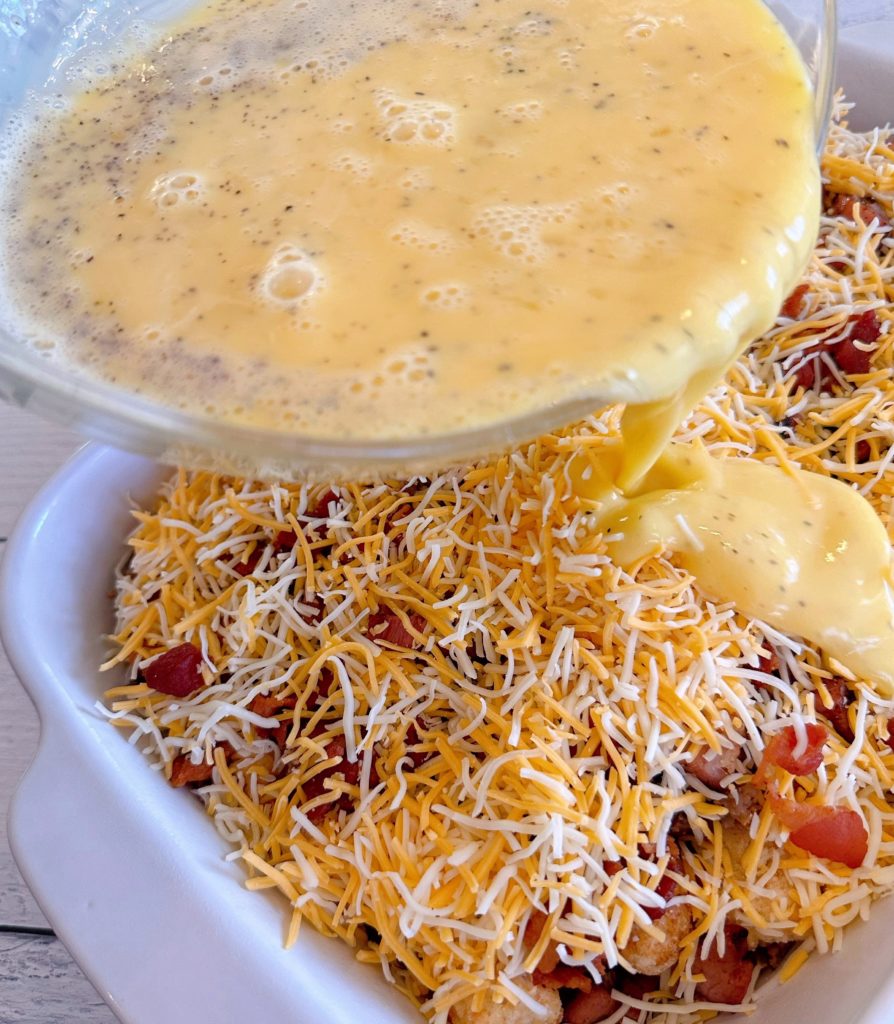 Pouring egg mixture over tater tots and meats in casserole dish.