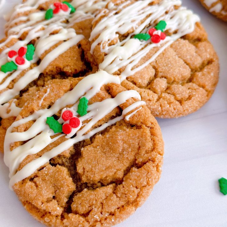 Gingersnap Molasses Cookies drizzled with white chocolate and a few sprinkles on a white counter.