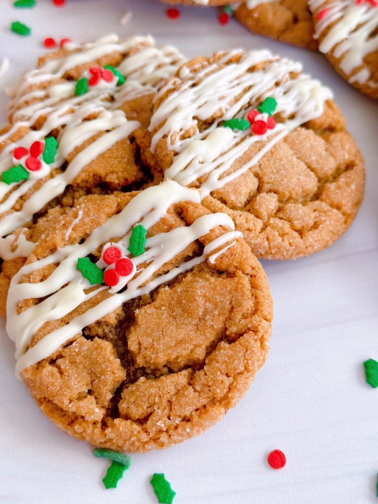 Gingersnap Molasses Cookies drizzled with white chocolate and a few sprinkles on a white counter.