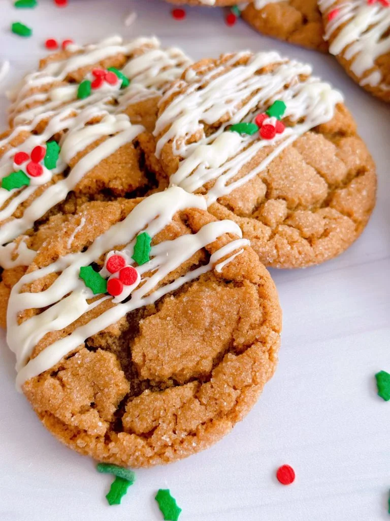 Gingersnap Molasses Cookies drizzled with white chocolate and a few sprinkles on a white counter.
