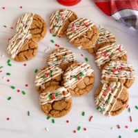 Gingersnap Molasses Cookies on a white counter drizzled with white chocolate and sprinkled with holiday sprinkles.