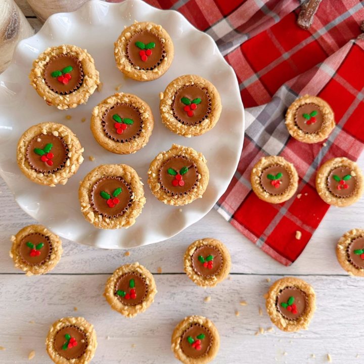 Overhead shot of Christmas Peanut Butter Cup cookies on a white cake plate and a plaid dish cloth.