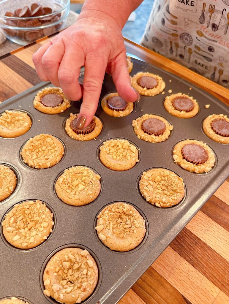 Placing reese's peanut cup into the center of each baked peanut butter cookie while in the mini muffin tin.