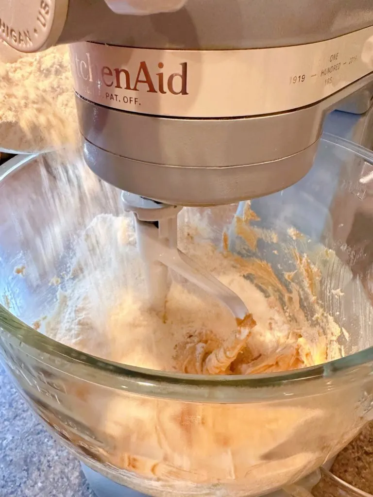 Adding flour and dry ingredients into creamed ingredients to make cookie dough.