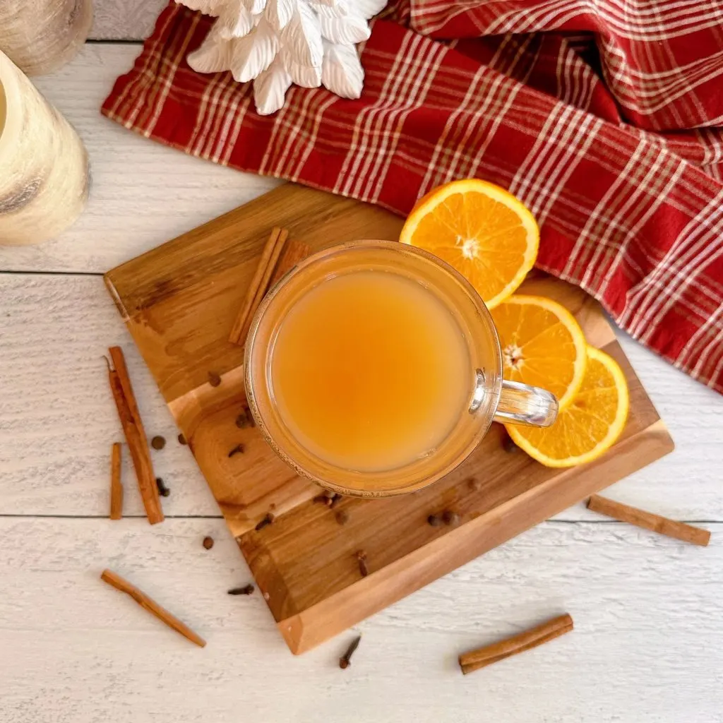 Spiced Cider in a mug on a board with spices and orange slices surrounding it.