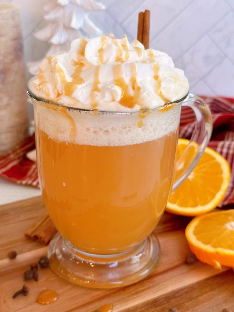 Close-up shot of Spiced Caramel Apple Hot Cider in a clear mug with whipped cream and caramel drizzle.