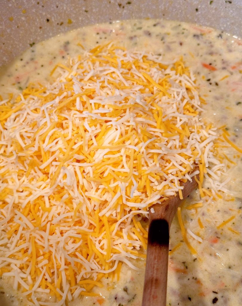Adding shredded cheddar cheese to soup mixture.