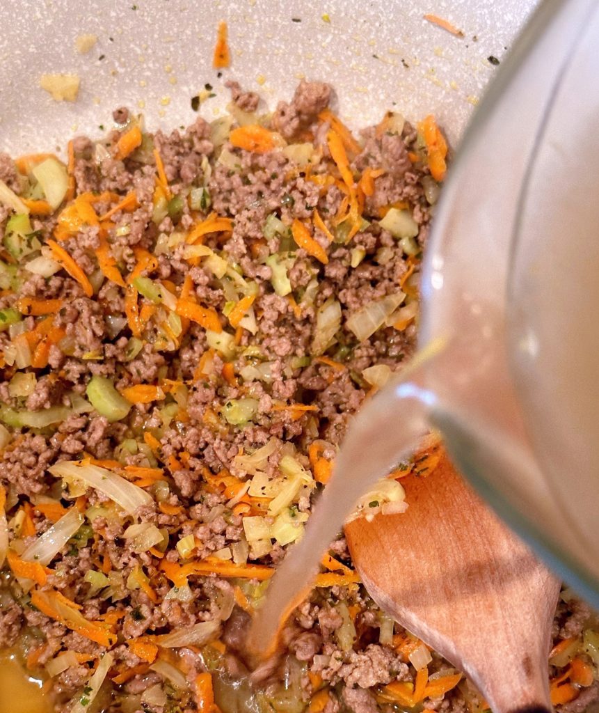 Adding chicken broth to ground beef and vegetable mixture.