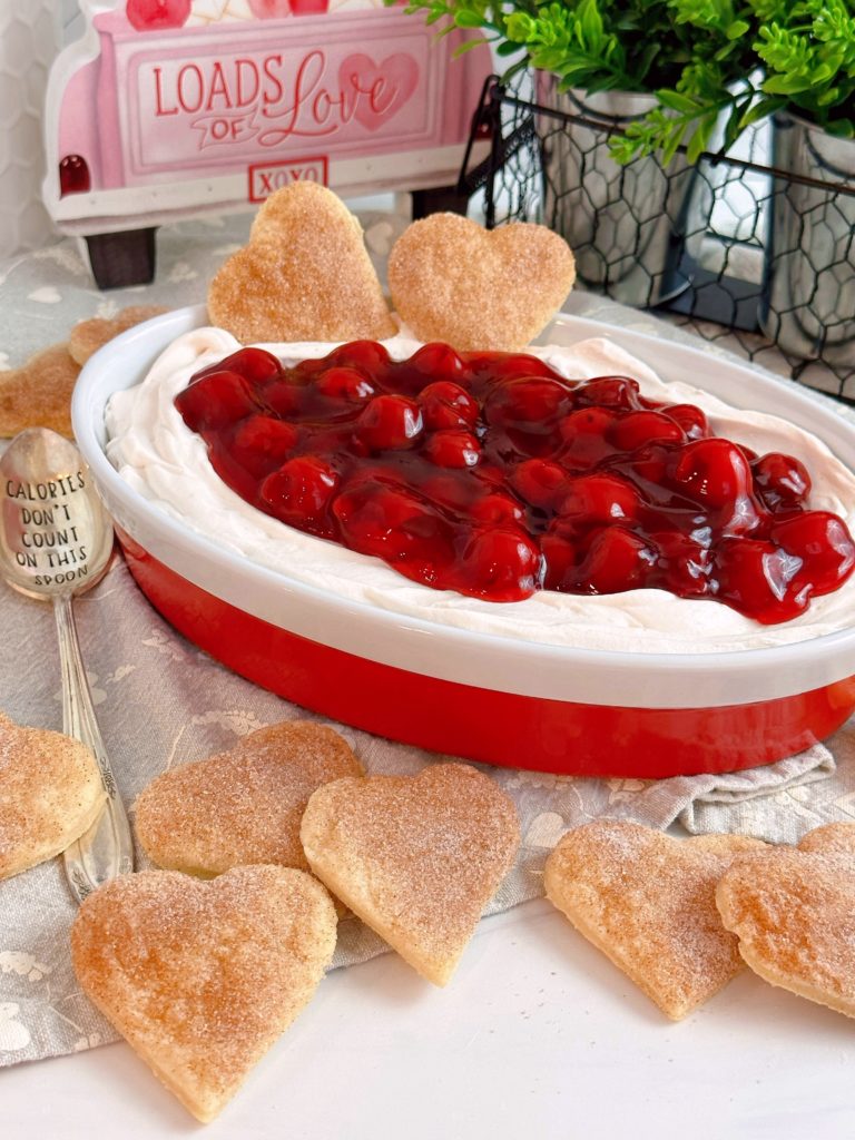 Red and white serving bowl filled with Cherries on a cloud dip with pie pastry hearts surrounding it.