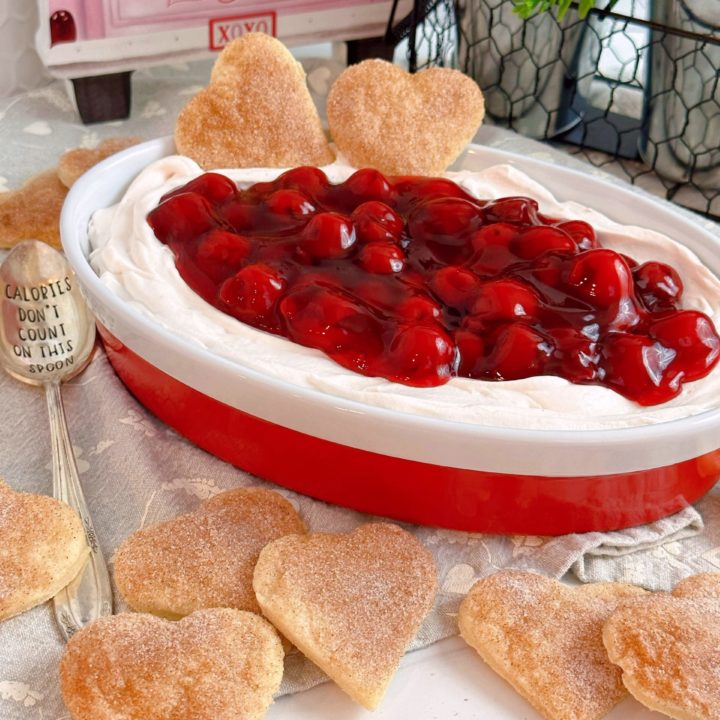 Red and white serving bowl filled with Cherries on a cloud dip with pie pastry hearts surrounding it.