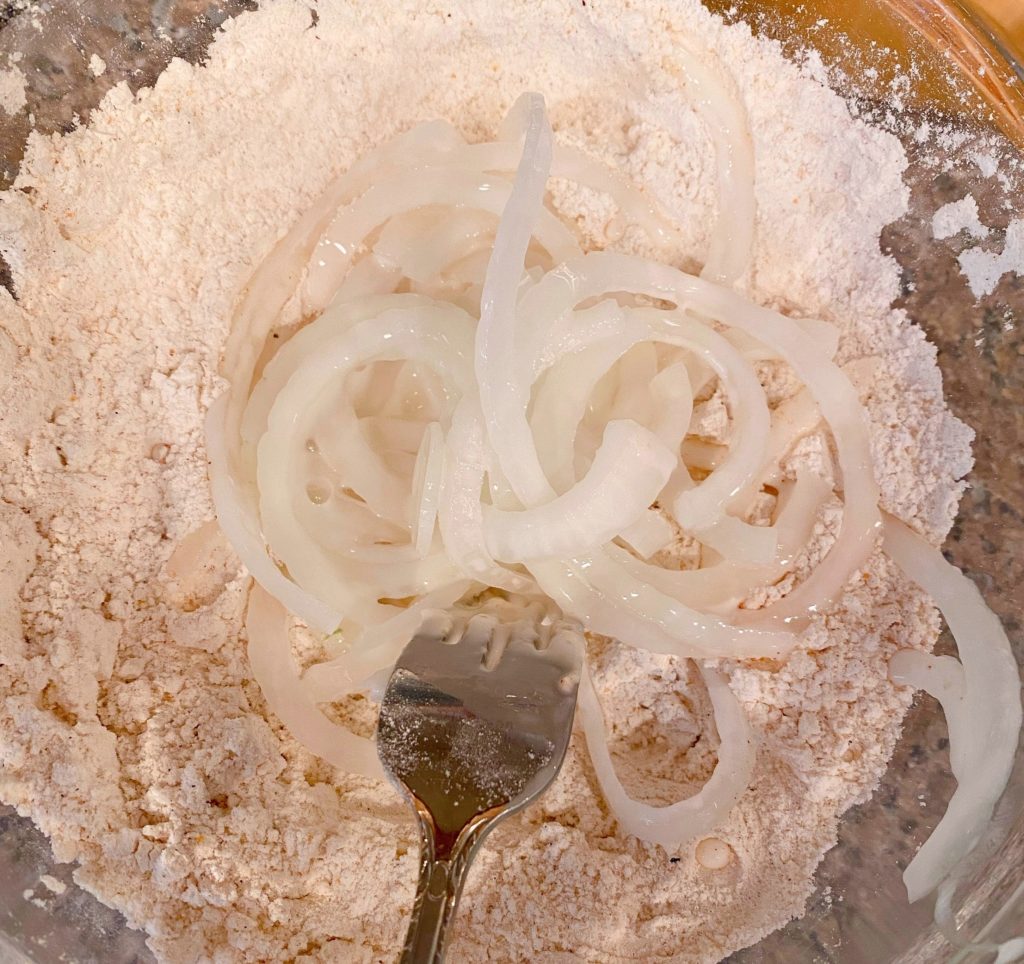 Onion straws being dredged in the flour mixture.