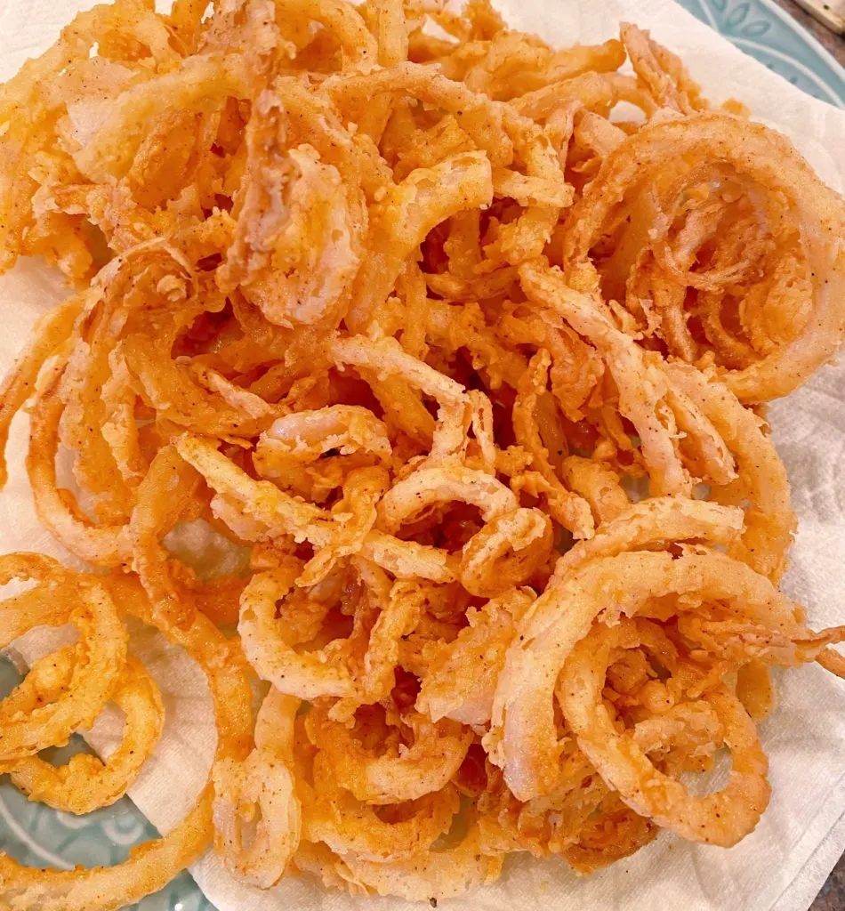 Fried Crispy Onion Straws on a paper towel lined plate.