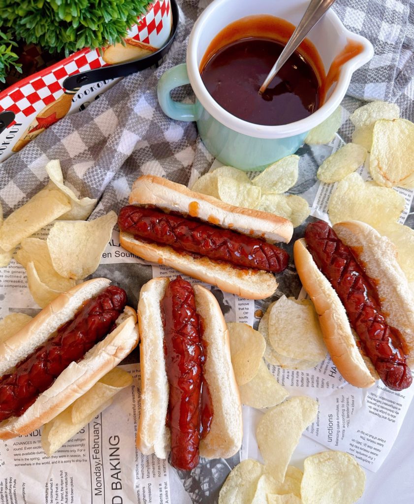 J. Dawgs on a table in buns with special sauce and a measuring cup with extra sauce.