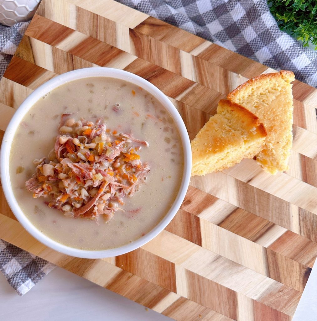 Overhead shot of Navy Bean Soup in a white bowl with two slices of corn bread on a cutting board.