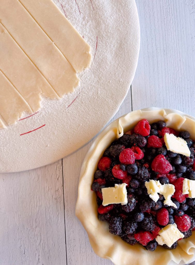 Top crust cut into vertical slats for lattice top crust. Pie sitting next to it waiting for crust topping to be added.