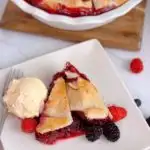 A slice of Triple Berry Deep Dish Galette on a white plate with a scoop of vanilla ice cream.