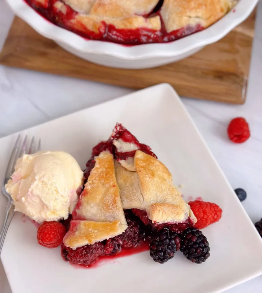 A slice of Triple Berry 
Deep Dish Galette on a white plate with a scoop of vanilla ice cream.