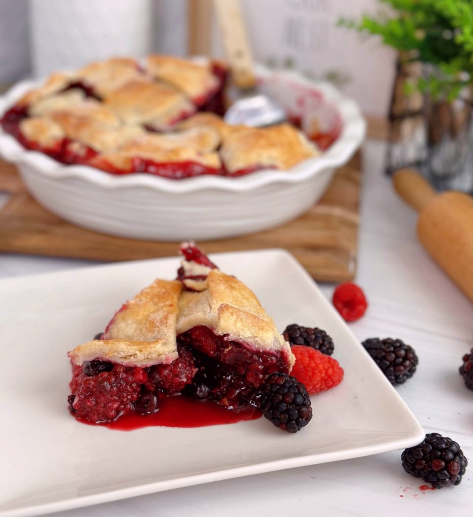 Triple Berry Galette in the background with a slice of the galette in the front on a white plate with berries all around it.