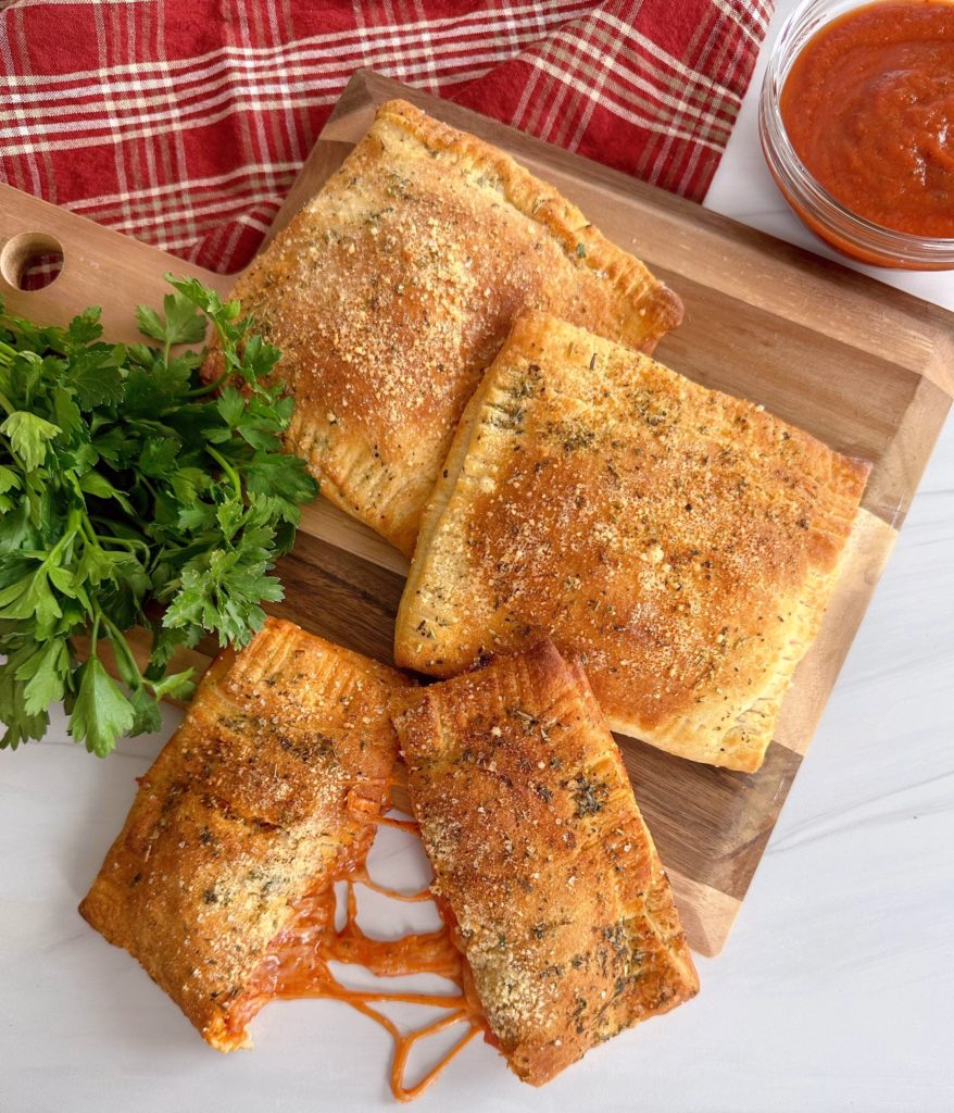Air Fryer Calzones on a wooden board with Italian Parsley and dipping sauce.
