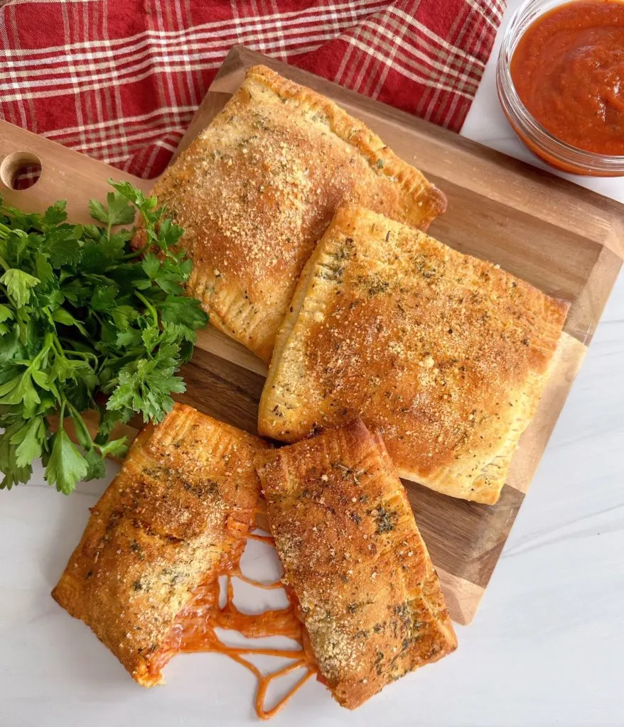 Air Fryer Calzones on a wooden board with Italian Parsley and dipping sauce.