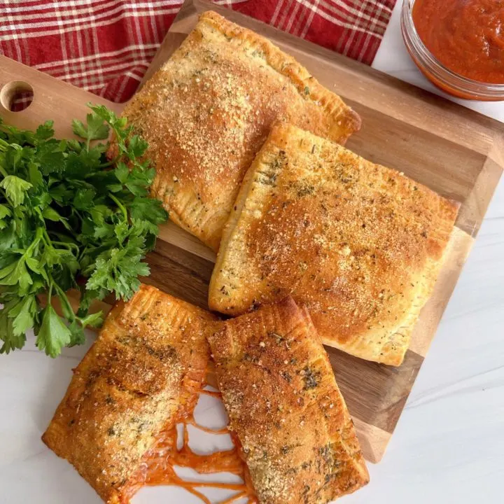 Air Fryer Calzones on a wooden board with Italian Parsley and dipping sauce.