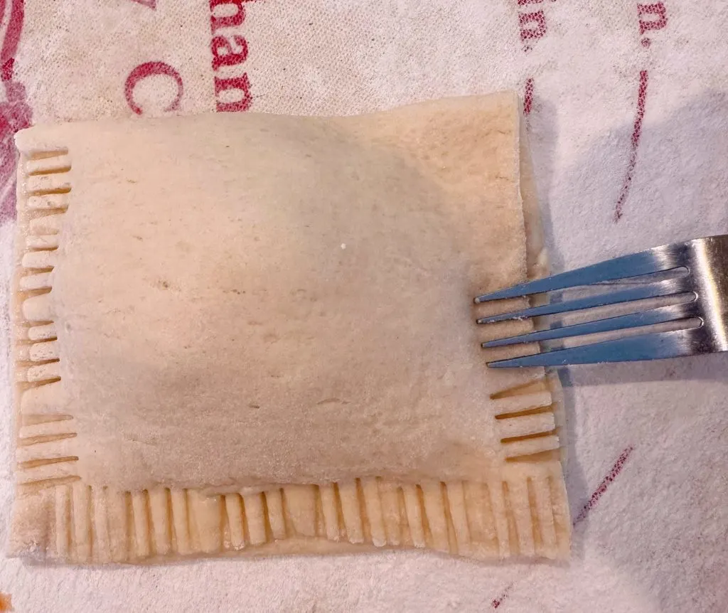 Using a fork to press down the edges of the calzone to seal them together.