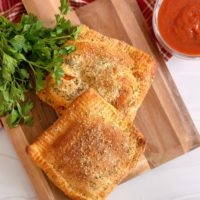 Overhead photo of Air Fryer Calzones, two of them, on a wooden board.