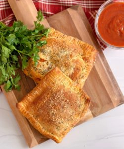 Overhead photo of Air Fryer Calzones, two of them, on a wooden board.