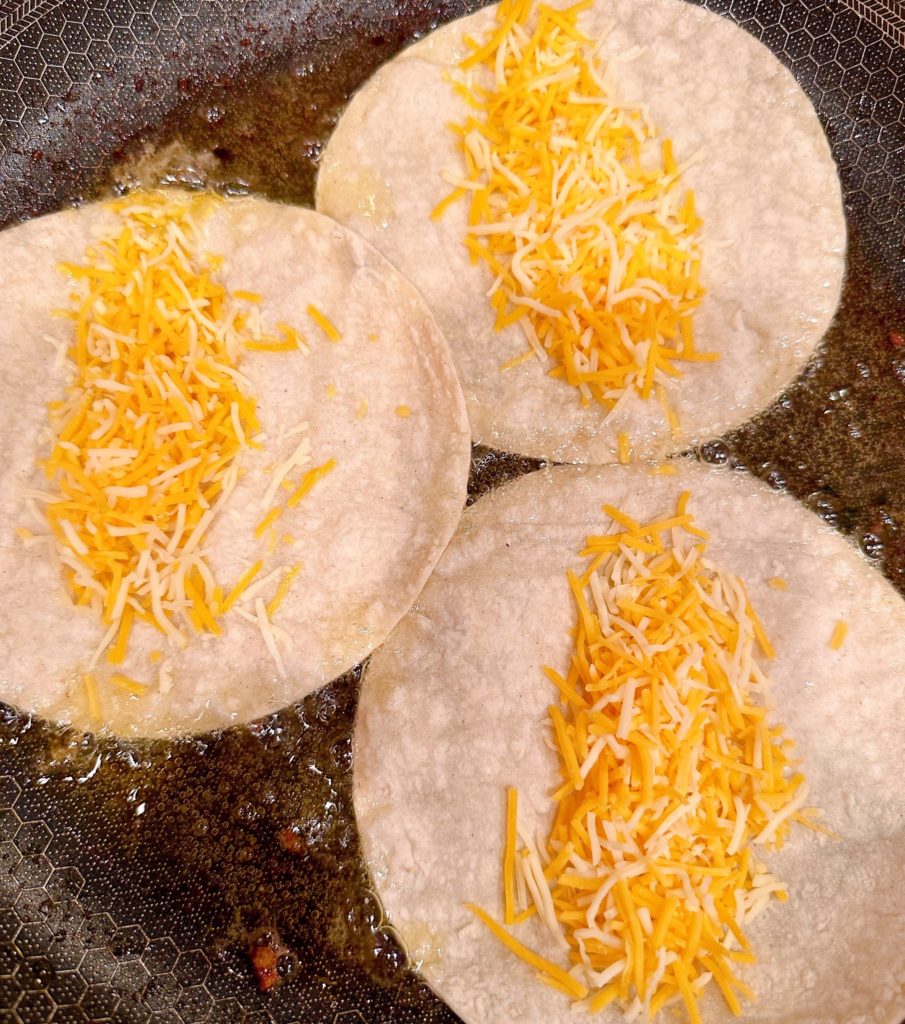 Adding cheese to corn tortillas in a skillet.