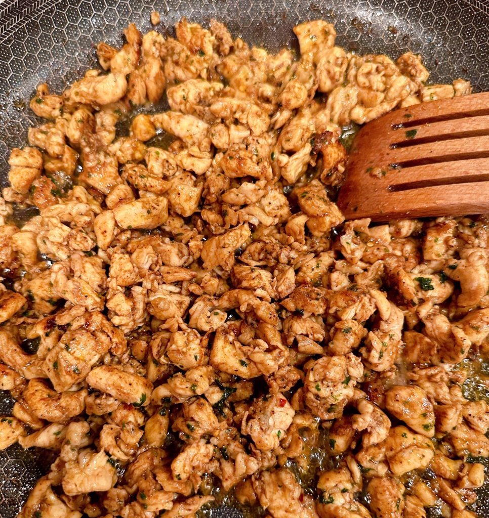 Cooking seasoned chicken in a large skillet on the stove.