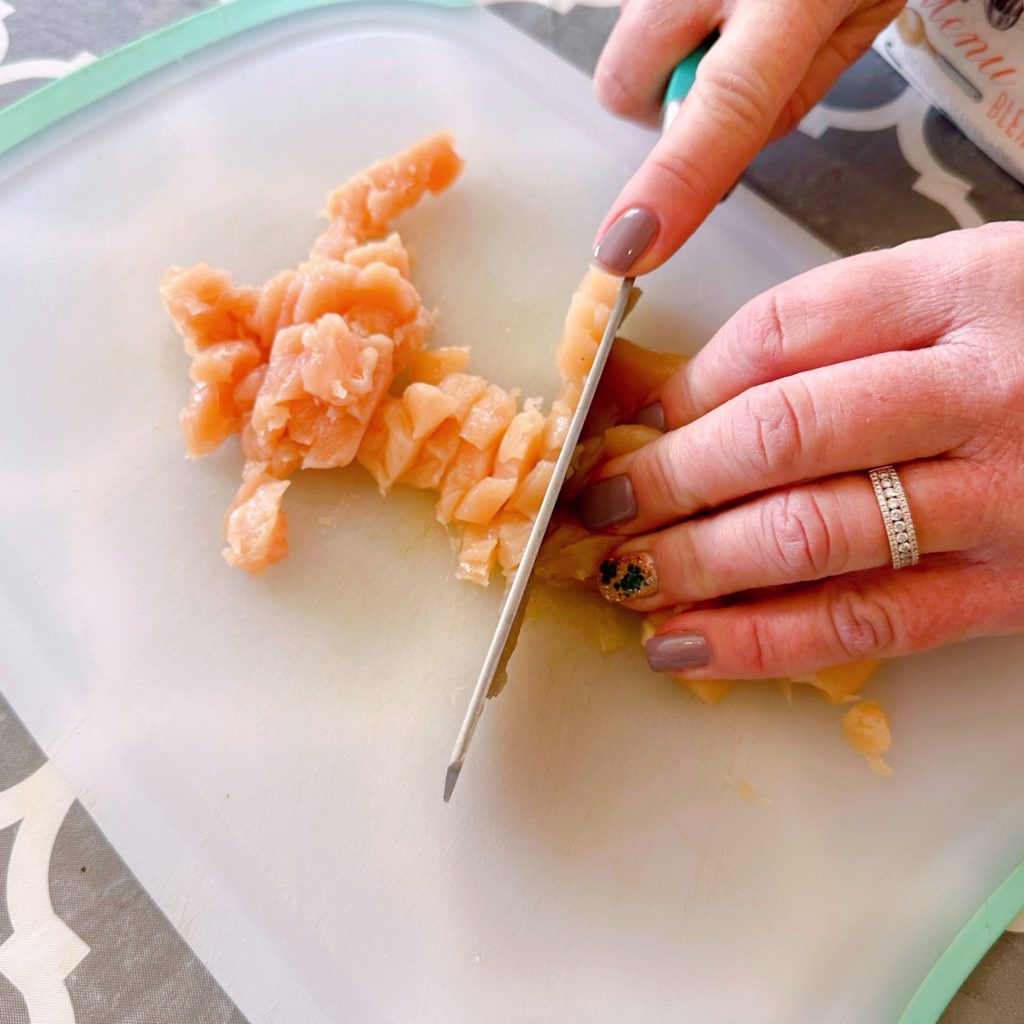 Cutting chicken tenders on a cutting board with a large knife.