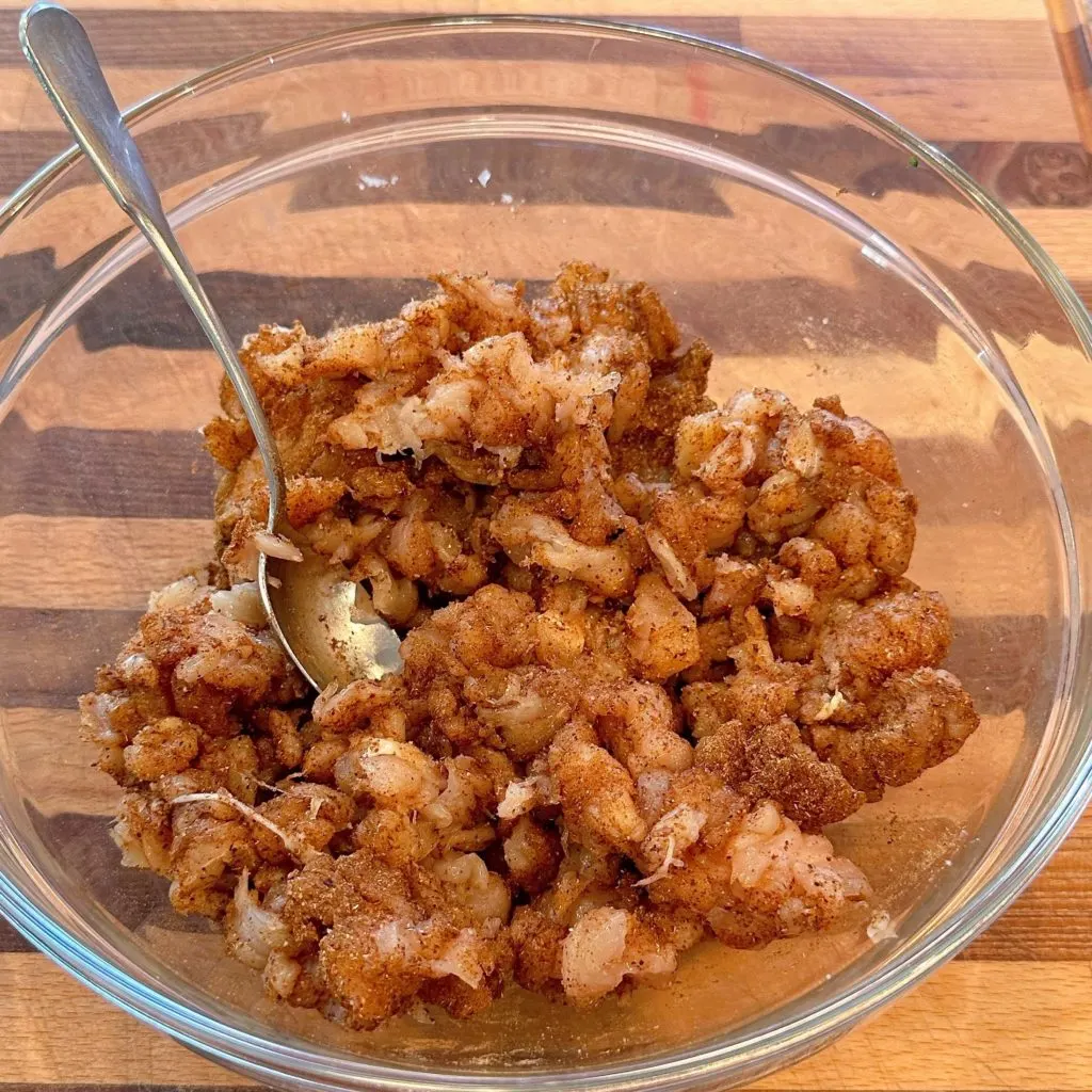 Diced Chicken meat in a large glass bowl seasoned with seasonings.