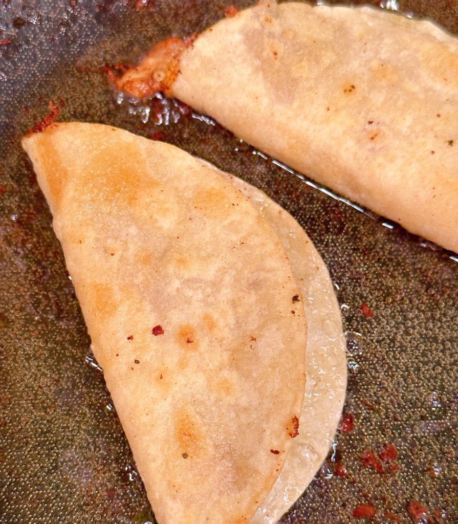 Tacos in a skillet being cooked once folded in half.