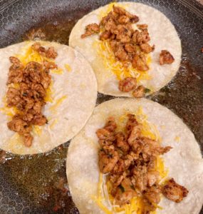 Adding chicken to the skillet tacos during frying.