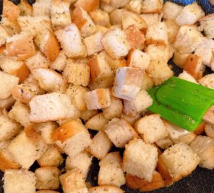 Cubed bread in a hot skillet being toasted with seasoned olive oil.