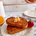 French Toast stacked with butter and Maple Syrup pouring over the top of them.