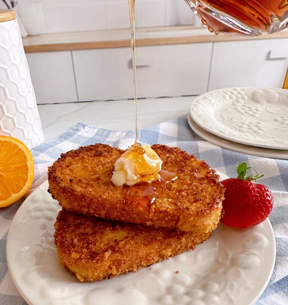 French Toast stacked with butter and Maple Syrup pouring over the top of them.