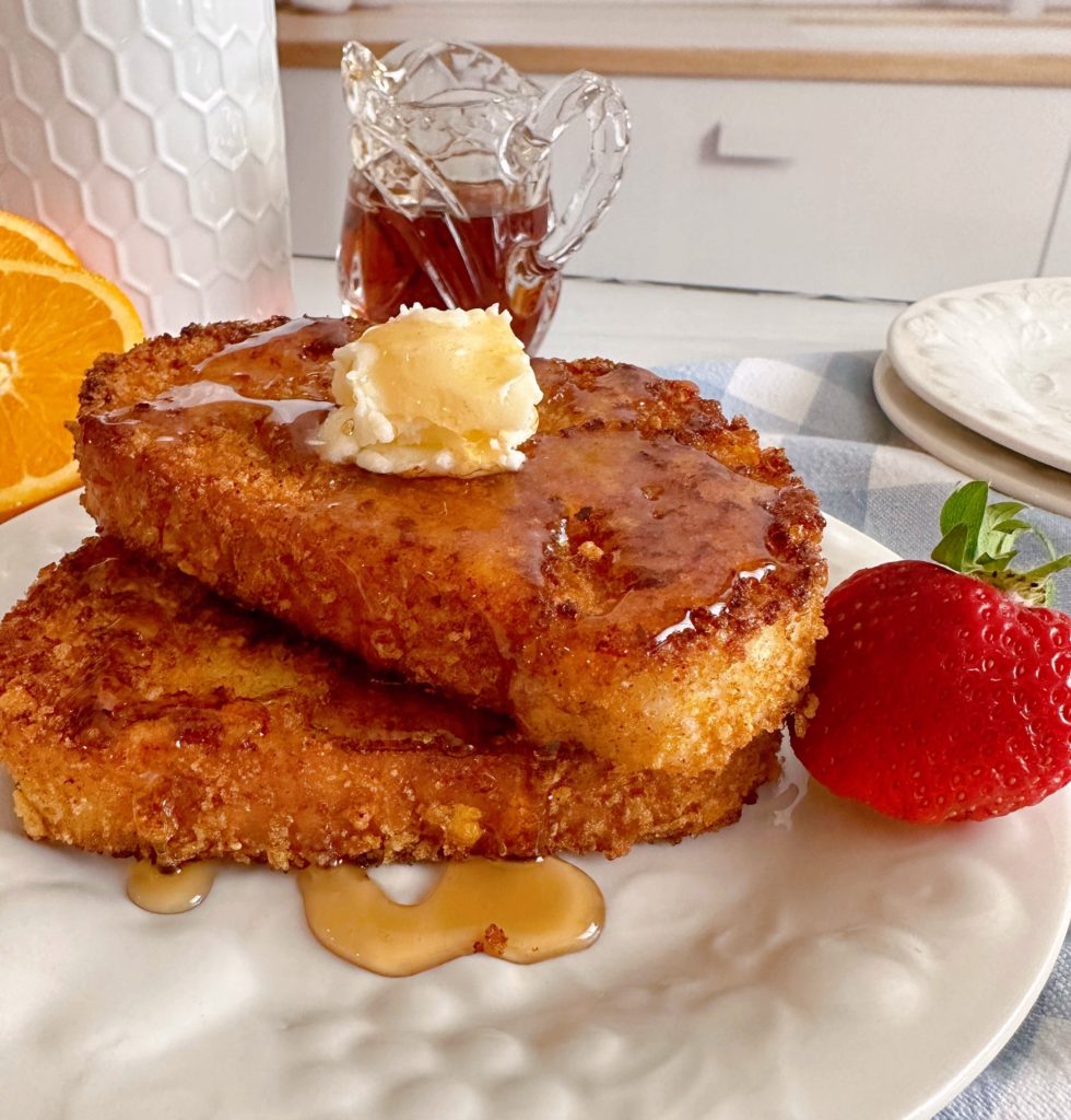 Two slices of Crispy Cinnamon Corn Flake French Toast stacked on top of each other with butter and maple syrup.